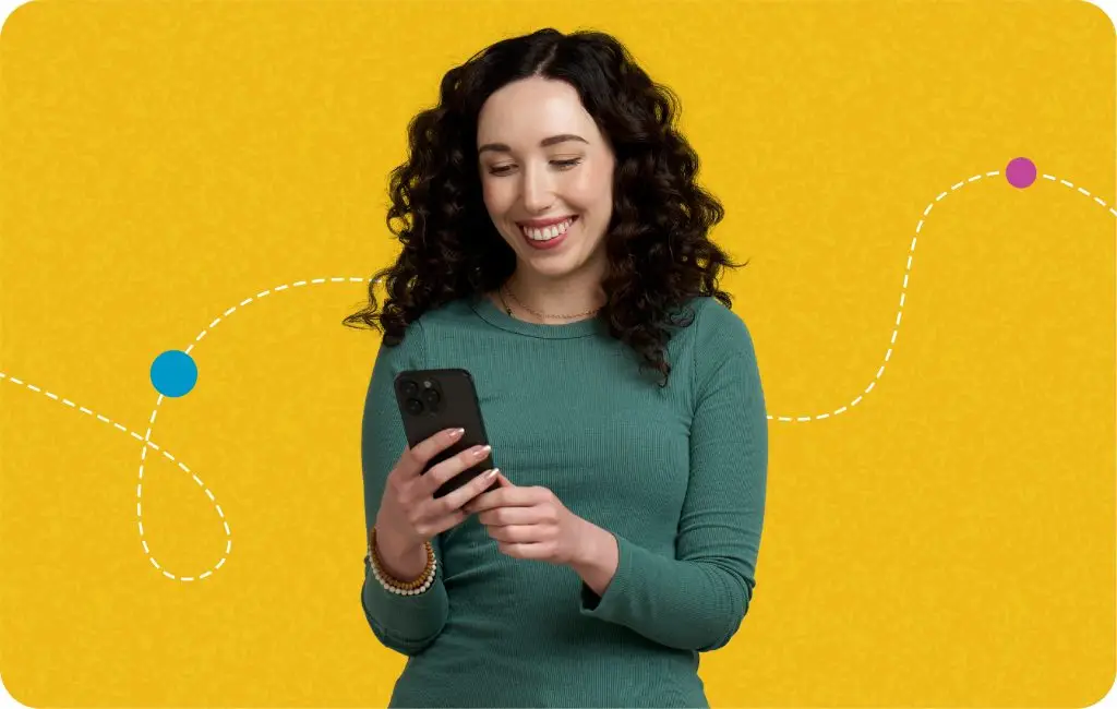 A woman with curly dark hair, wearing a green long-sleeve top, smiles while looking at her smartphone. The background is yellow with a dotted, curved line and two colorful dots.